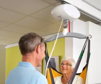 Male carer safely lifting a resident using the GH1 Q Lifting module on Wall rails in a nursing home setting.