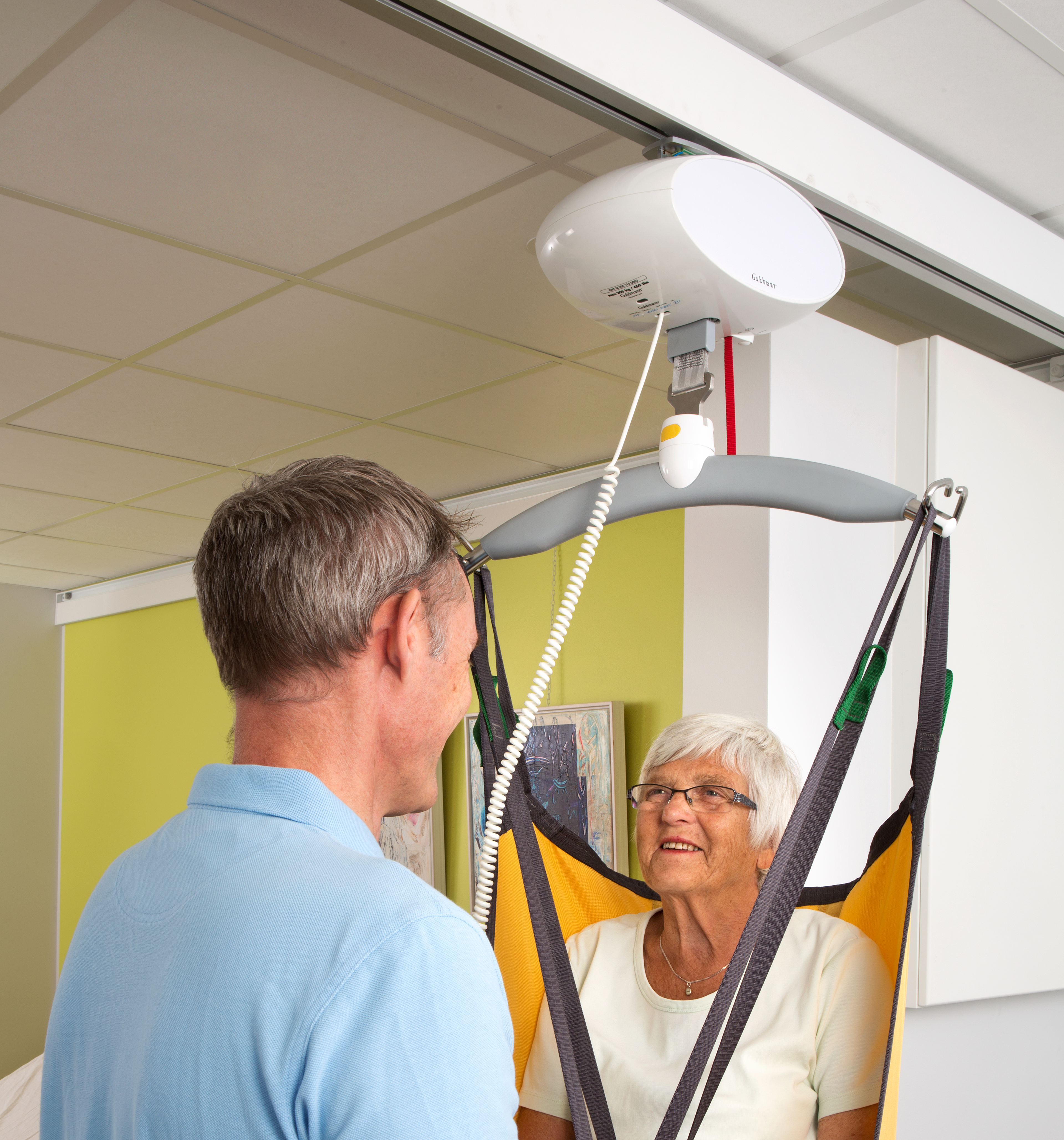 Male carer safely lifting a resident using the GH1 Q Lifting module on Wall rails in a nursing home setting.
