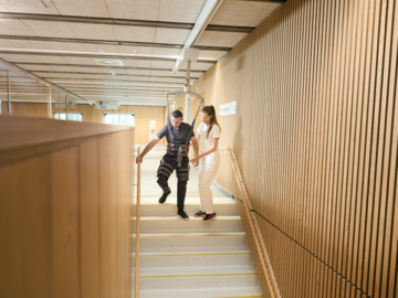 Patiënt daalt trappen af in een Gait Trainer tilband met GH3+ plafondlift – veilige neurorevalidatie in het Rigshospitalet met valbeveiliging.