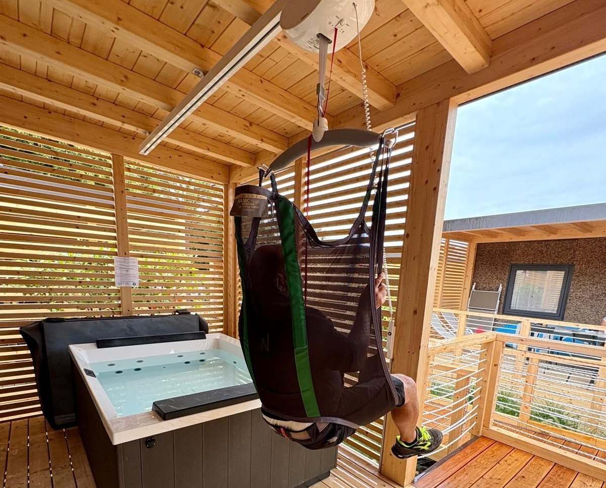 Guest using the Guldmann ceiling hoist to enter the hot tub, showcasing inclusive tourism at Camping Bergamini.