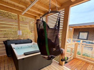 Guest using the Guldmann ceiling hoist to enter the hot tub, showcasing inclusive tourism at Camping Bergamini.