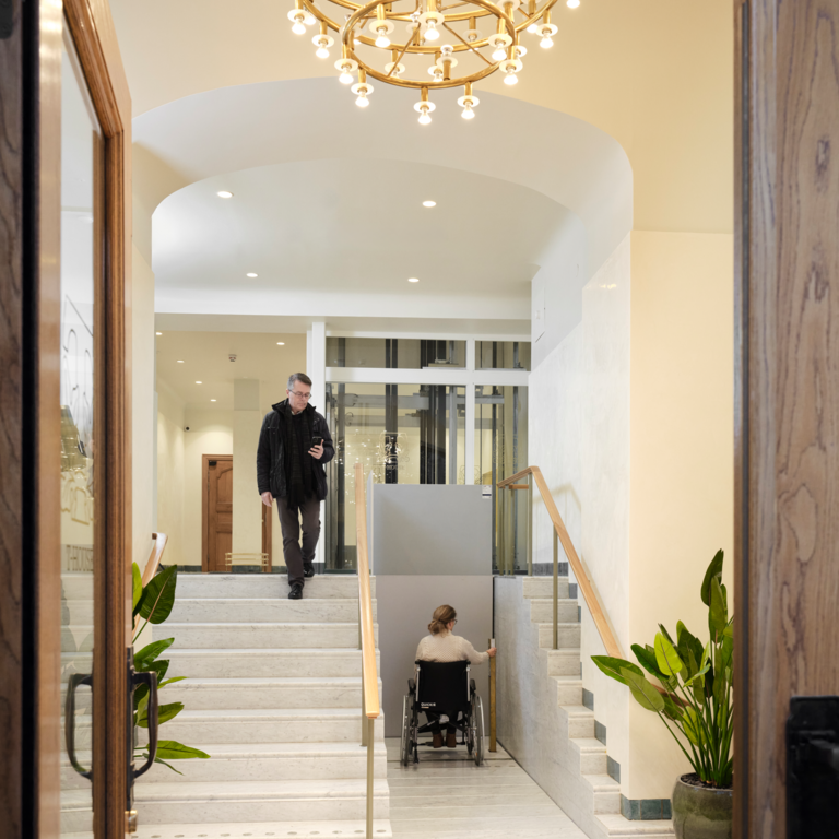 Rolstoelgebruiker gaat omhoog op Stepless SLP model C platformlift naast trap in T-House
